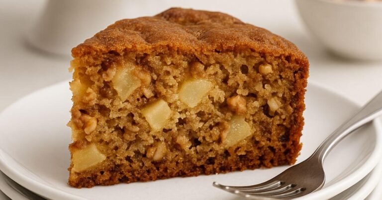 Close-up of a moist apple cake slice with fresh apple chunks and walnuts on a white plate.