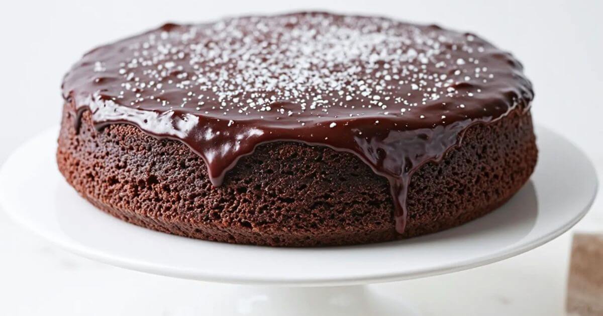 Small chocolate cake with glossy ganache topping and powdered sugar on a white plate