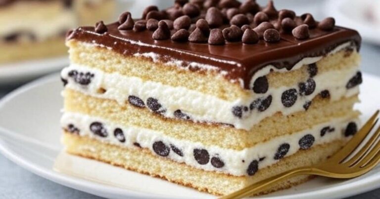 A close-up slice of Cannoli Cake featuring layers of soft sponge, creamy chocolate chip filling, and a glossy chocolate ganache topping, served with a gold fork on a white dessert plate.