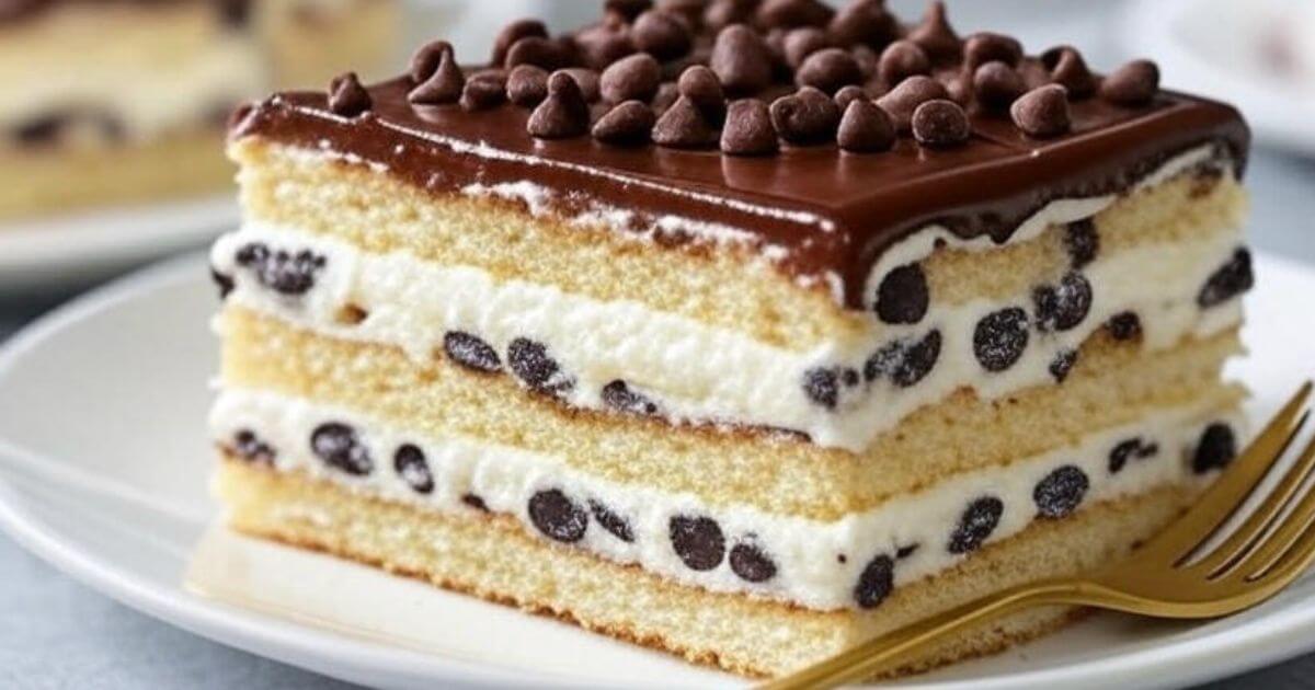 A close-up slice of Cannoli Cake featuring layers of soft sponge, creamy chocolate chip filling, and a glossy chocolate ganache topping, served with a gold fork on a white dessert plate.