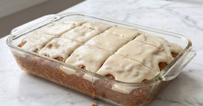 Freshly baked moist apple spice cake with smooth vanilla glaze icing sliced into squares inside a glass baking dish.