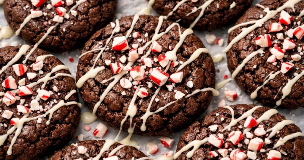 Close-up of Peppermint Brownie Cookies drizzled with white chocolate and topped with crushed candy canes on a baking sheet.