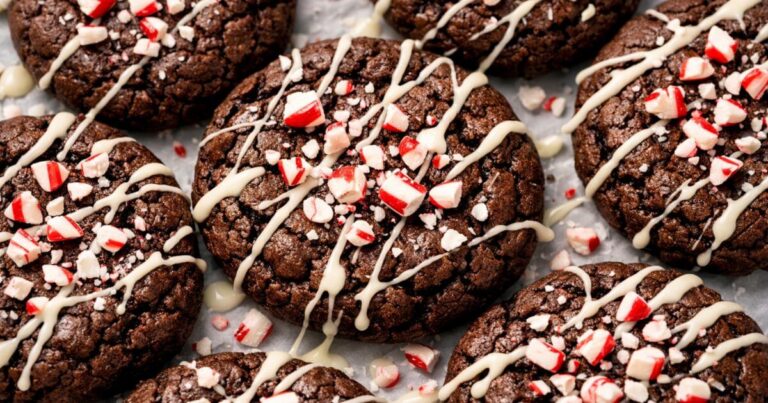 Close-up of Peppermint Brownie Cookies drizzled with white chocolate and topped with crushed candy canes on a baking sheet.