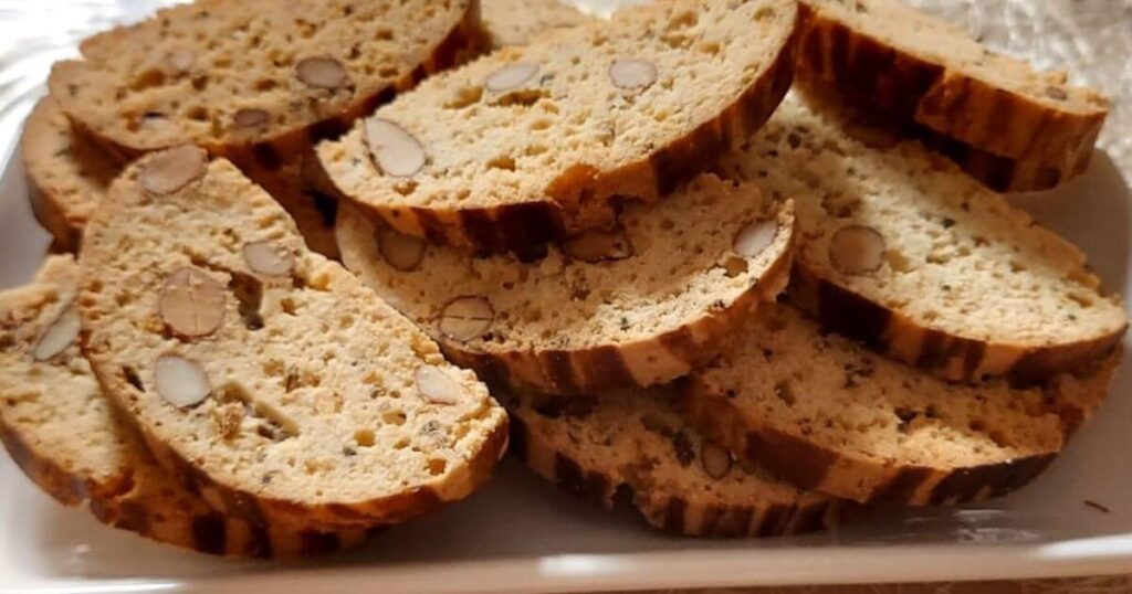 Slices of golden-brown Moroccan Fekkas with whole almonds on a white plate, showcasing the crunchy texture of this traditional Moroccan biscotti.