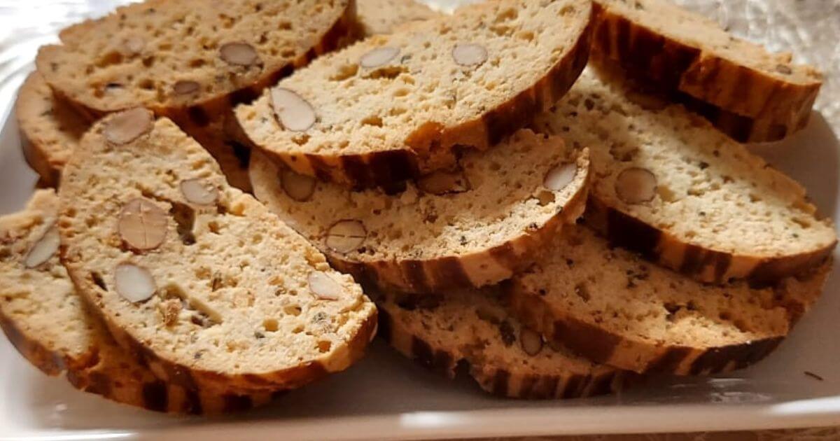 Slices of golden-brown Moroccan Fekkas with whole almonds on a white plate, showcasing the crunchy texture of this traditional Moroccan biscotti.