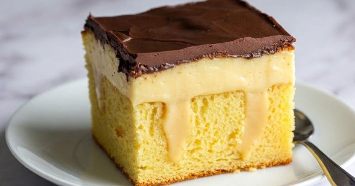 A close-up square slice of Boston Cream Poke Cake on a white plate, showing the yellow sponge cake layer, creamy vanilla pudding seeping into the pokes, and a smooth chocolate ganache topping.