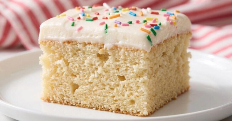 slice of the best vanilla sheet cake with fluffy buttercream frosting and colorful rainbow sprinkles, served on a white plate.