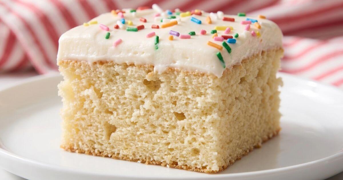 slice of the best vanilla sheet cake with fluffy buttercream frosting and colorful rainbow sprinkles, served on a white plate.