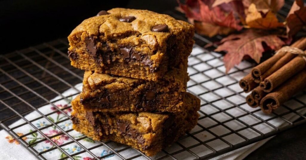 Stack of chewy pumpkin chocolate chip bars on a wire cooling rack with cinnamon sticks and fall leaves