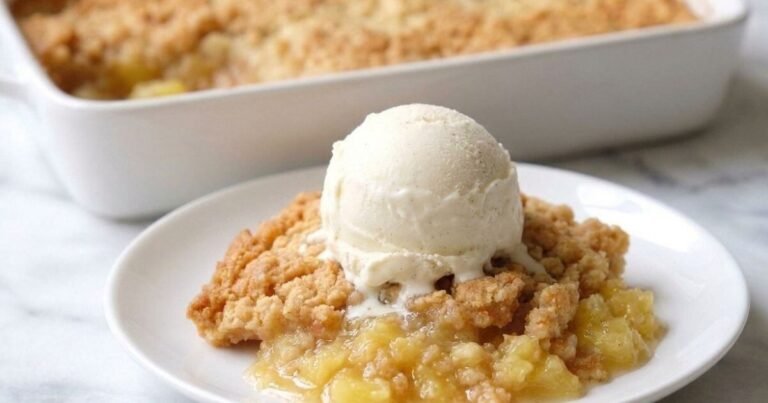 Serving of pineapple dump cake recipe topped with vanilla ice cream on a white plate